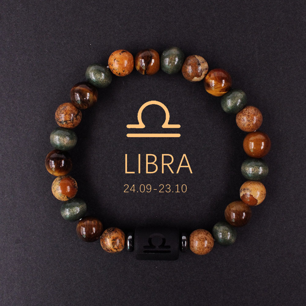 Natural zodiac stone bracelet resting on dark wood beside a leather watch and linen cloth, soft daylight, masculine grounded zodiac atmosphere, handmade crystal jewelry.