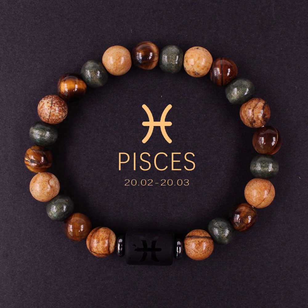 Natural zodiac stone bracelet resting on dark wood beside a leather watch and linen cloth, soft daylight, masculine grounded zodiac atmosphere, handmade crystal jewelry.