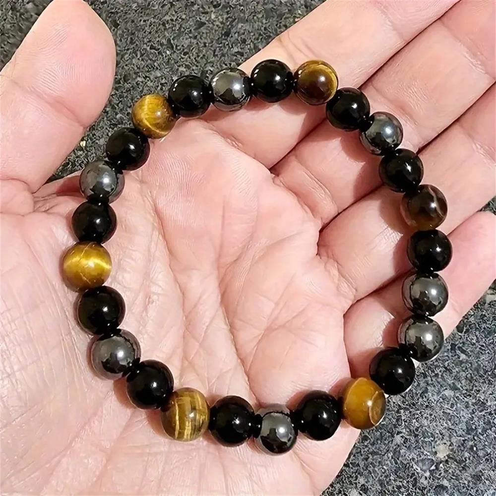 Natural tiger eye obsidian hematite bracelet resting on linen beside a small brass bowl, soft daylight showing the three distinct stone tones side by side
