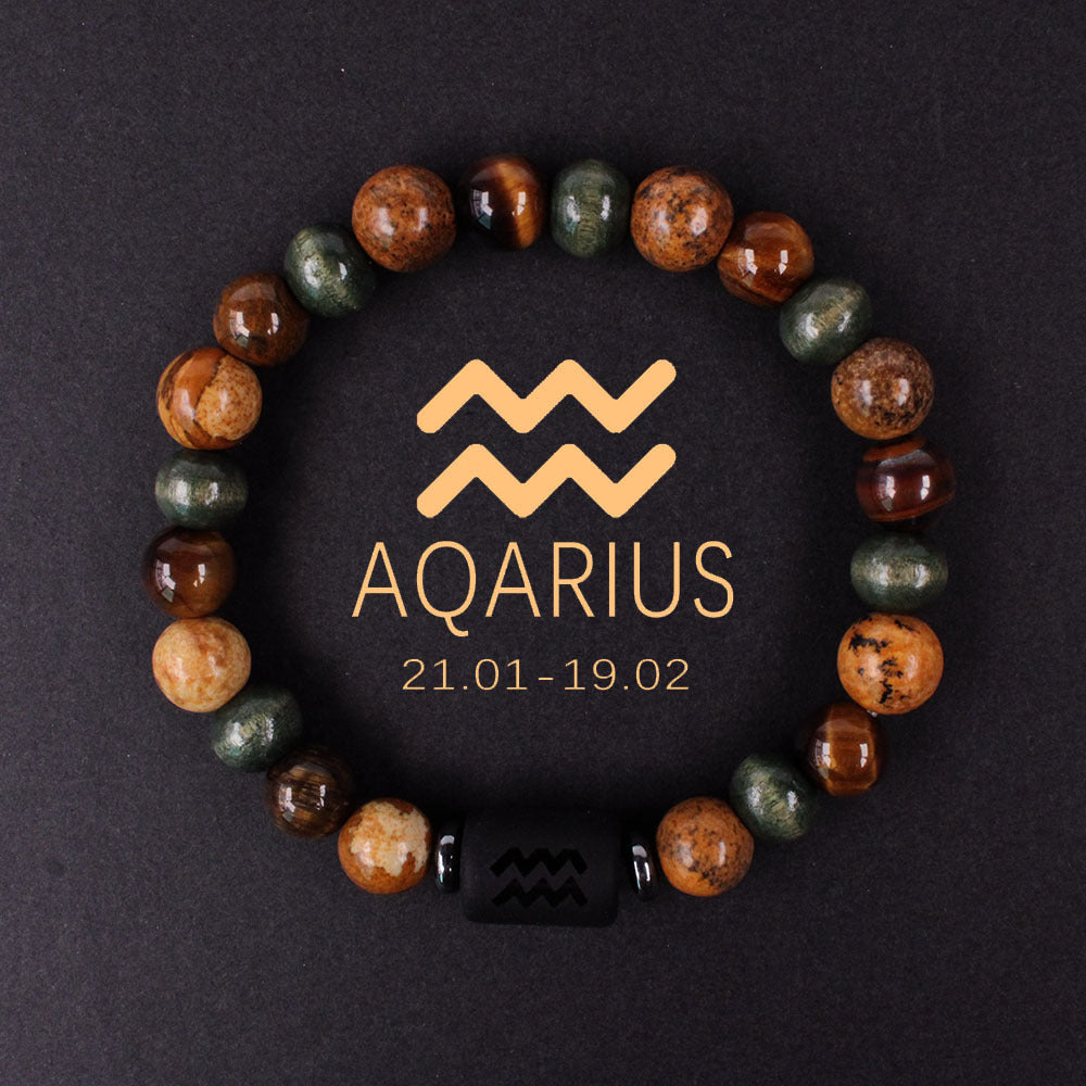 Natural zodiac stone bracelet showing three-color alternating beads — warm chatoyant tiger eye, blue-green hawk eye and dark agate — with engraved black obsidian zodiac symbol charm on elastic cord.