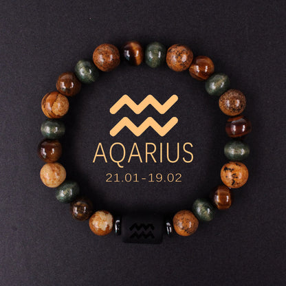 Natural zodiac stone bracelet showing three-color alternating beads — warm chatoyant tiger eye, blue-green hawk eye and dark agate — with engraved black obsidian zodiac symbol charm on elastic cord.
