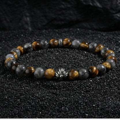 Natural tiger eye hawk eye stone bracelet resting on dark wood beside a leather watch and linen cloth, soft daylight, masculine grounded everyday atmosphere, handmade crystal jewelry for men.