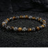 Natural tiger eye hawk eye stone bracelet resting on dark wood beside a leather watch and linen cloth, soft daylight, masculine grounded everyday atmosphere, handmade crystal jewelry for men.