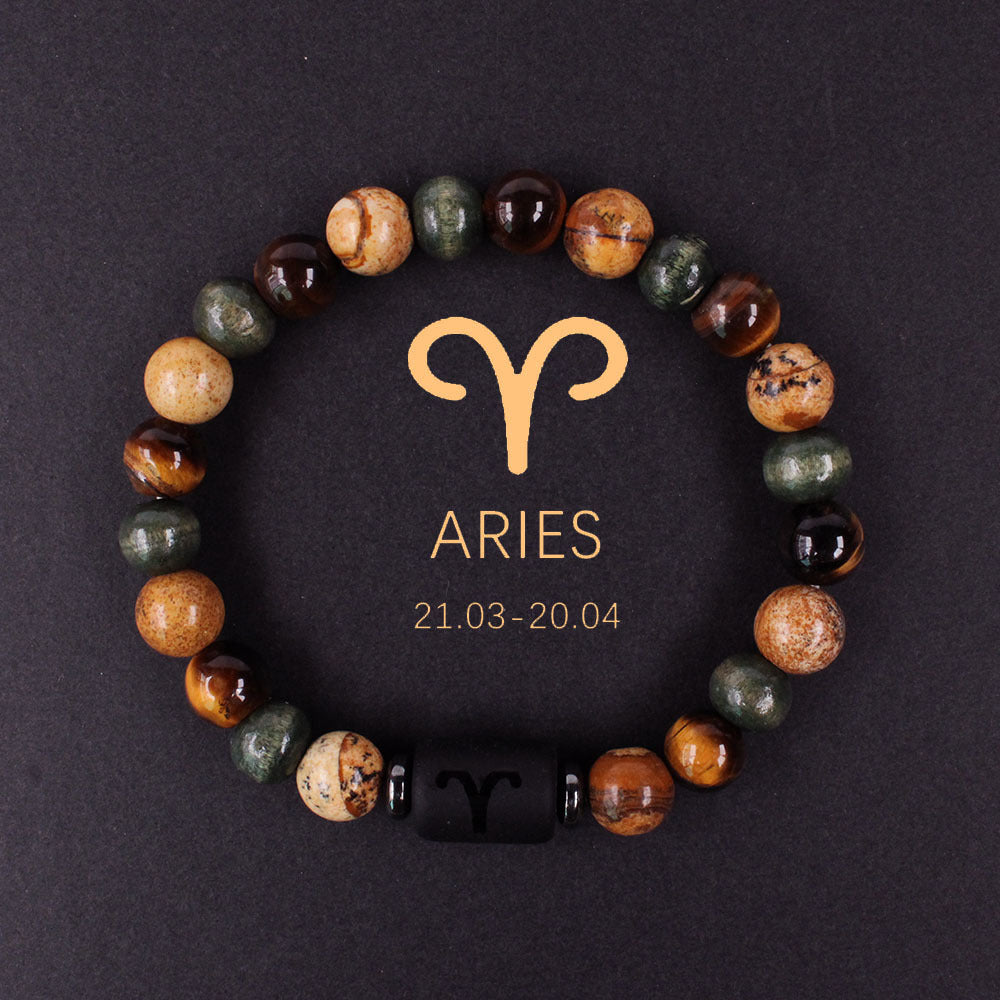 Natural zodiac stone bracelet showing three-color alternating beads — warm chatoyant tiger eye, blue-green hawk eye and dark agate — with engraved black obsidian zodiac symbol charm on elastic cord.