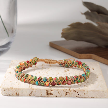 Close-up of Multi-Color Gemstone Woven Bracelet showing hand-knotted golden cord weaving between red, pink, amber, green, turquoise and ivory natural stone beads in macramé-style pattern.`