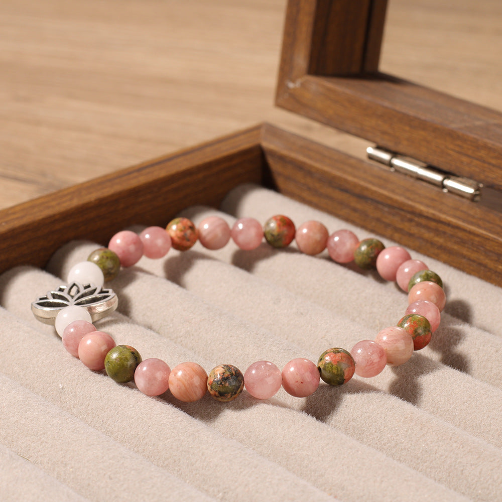 Close-up of Natural Pink Crystal Lotus Bracelet, focusing on the rose-toned stone beads, the red-green speckled accent beads and the silver lotus charm detail 