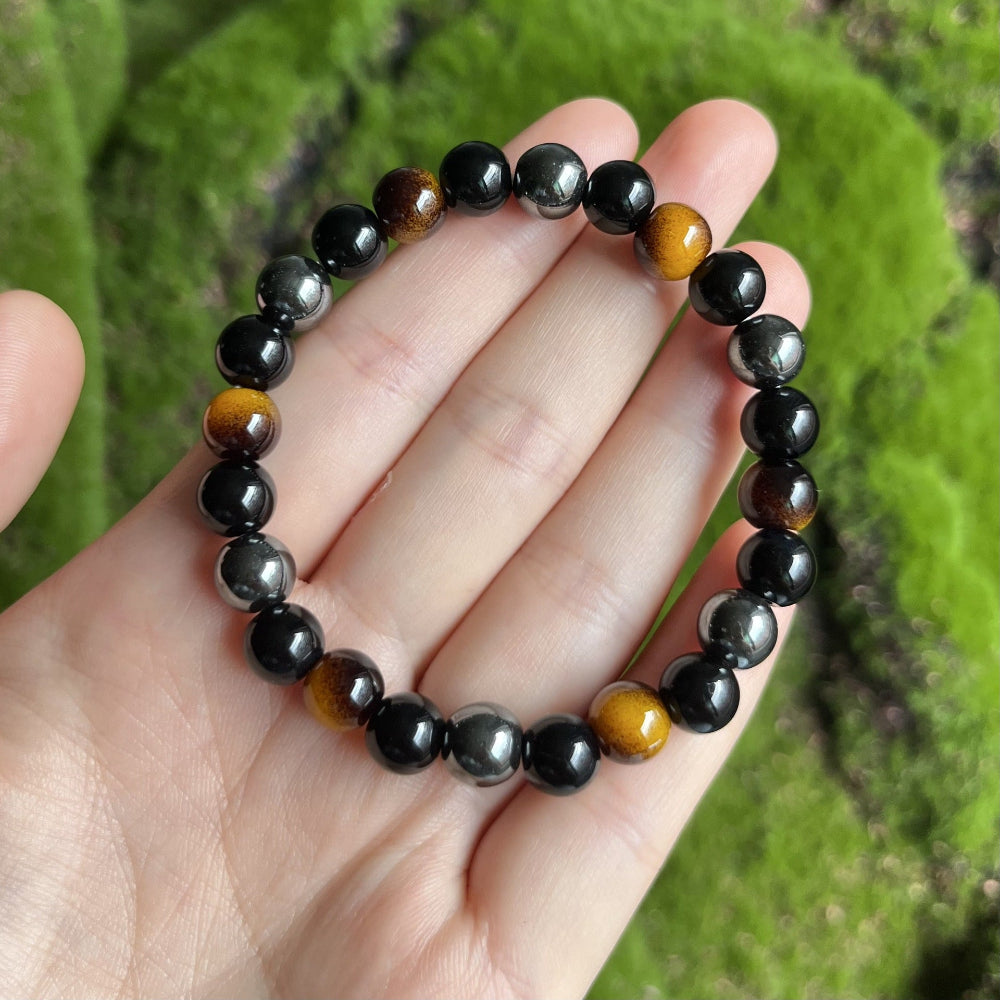 Close-up of natural tiger eye obsidian hematite bracelet detail of a single honey-banded tiger eye bead next to a deep mirror-black obsidian round and a polished hematite bead