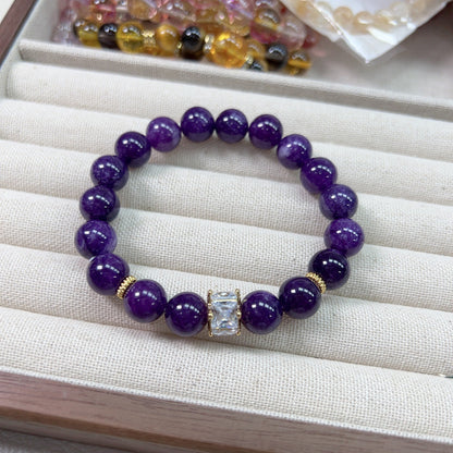 Close-up of natural amethyst bracelet beads showing 8mm polished round surface with cloud-like veining inclusions, deep violet tone with natural pattern uniqueness per bead.