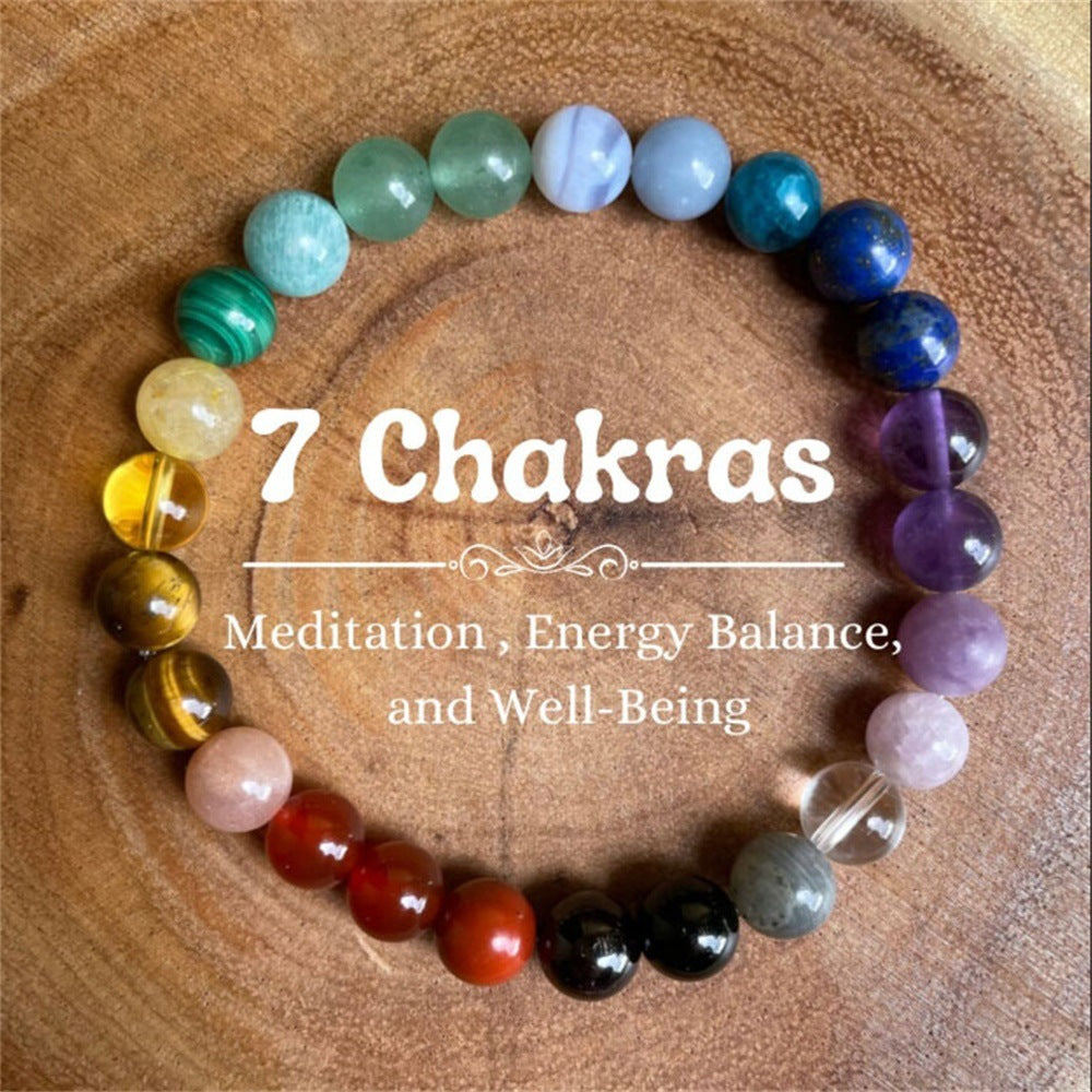  Multi-Color Natural Crystal Stone Bracelet on a warm wood surface, hand-strung with eighteen polished natural stone beads spanning yellow, pink, red, violet, blue, green and teal in one circle 