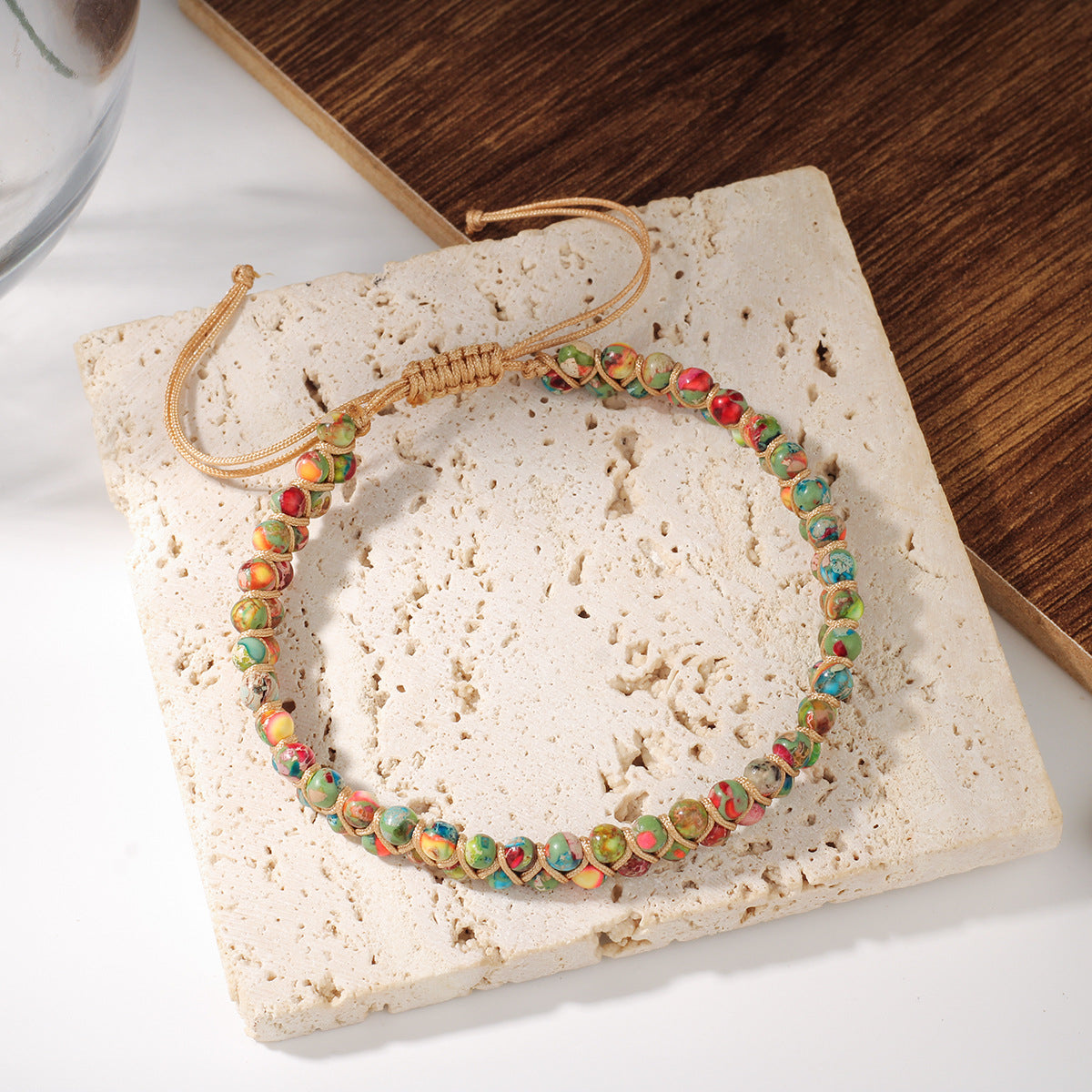 Close-up of Multi-Color Gemstone Woven Bracelet showing hand-knotted golden cord weaving between red, pink, amber, green, turquoise and ivory natural stone beads in macramé-style pattern.`