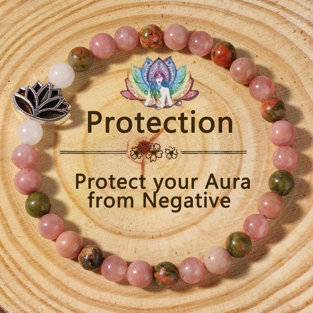 Natural Pink Crystal Lotus Bracelet on a warm wood plate, hand-strung with smooth rose-toned stone beads and a small silver lotus charm resting against the wrist