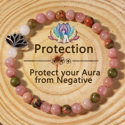 Natural Pink Crystal Lotus Bracelet on a warm wood plate, hand-strung with smooth rose-toned stone beads and a small silver lotus charm resting against the wrist