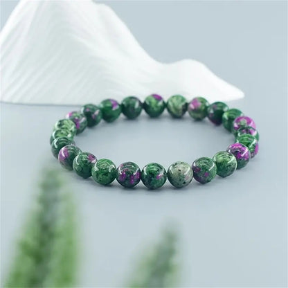 Natural Green Zoisite Ruby Bracelet on a warm wood plate, hand-strung with mottled green stone beads, black veining and small ruby-red mineral accents